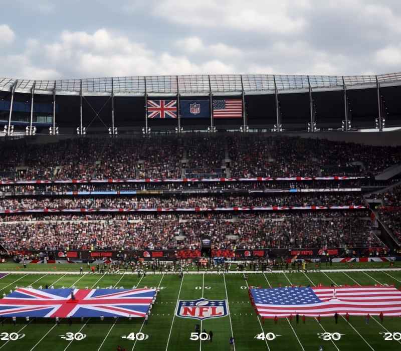 Packed stadium crowd with UK and USA flags displayed on the field before an NFL London game