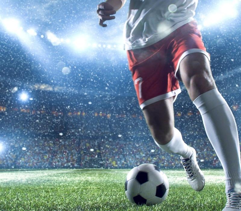 Close-up of a footballer's legs controlling the ball in a packed, illuminated stadium