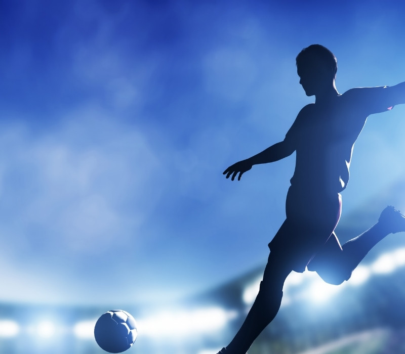 Dramatic silhouette of a footballer jumping in celebration on a blue-toned stadium backdrop