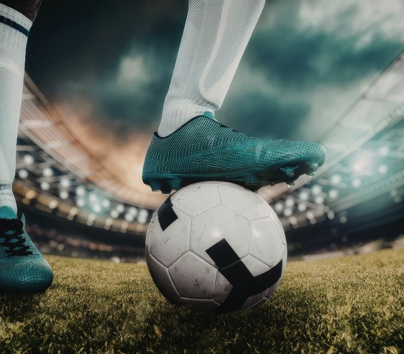 Close-up shot of a football boot on a soccer ball inside a stadium at dusk